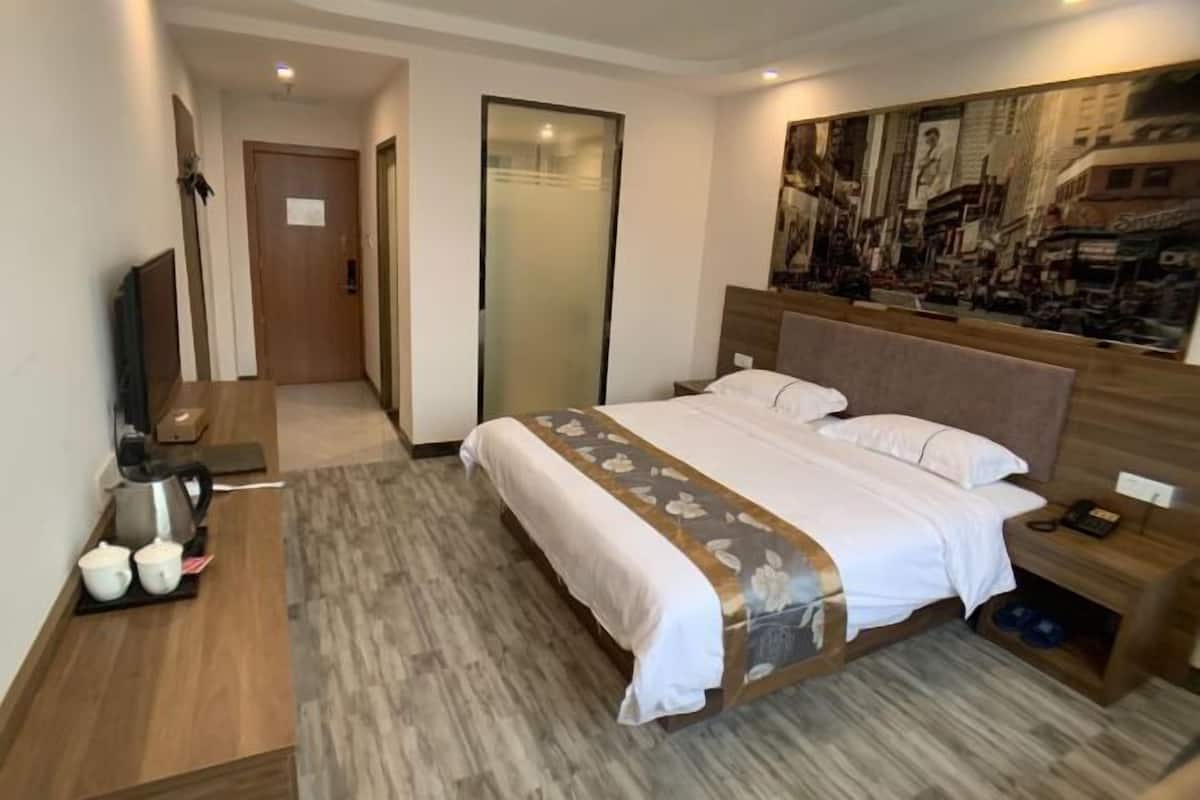 Une chambre d’hôtel avec un grand lit, un téléviseur à écran plat, une table de chevet en bois et un tableau au mur.