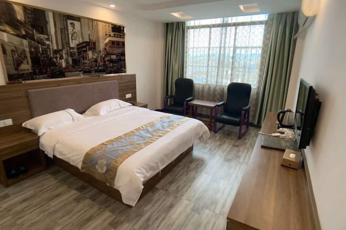 Une chambre d’hôtel avec un grand lit, un bureau, deux chaises, une télévision et un tableau au mur.