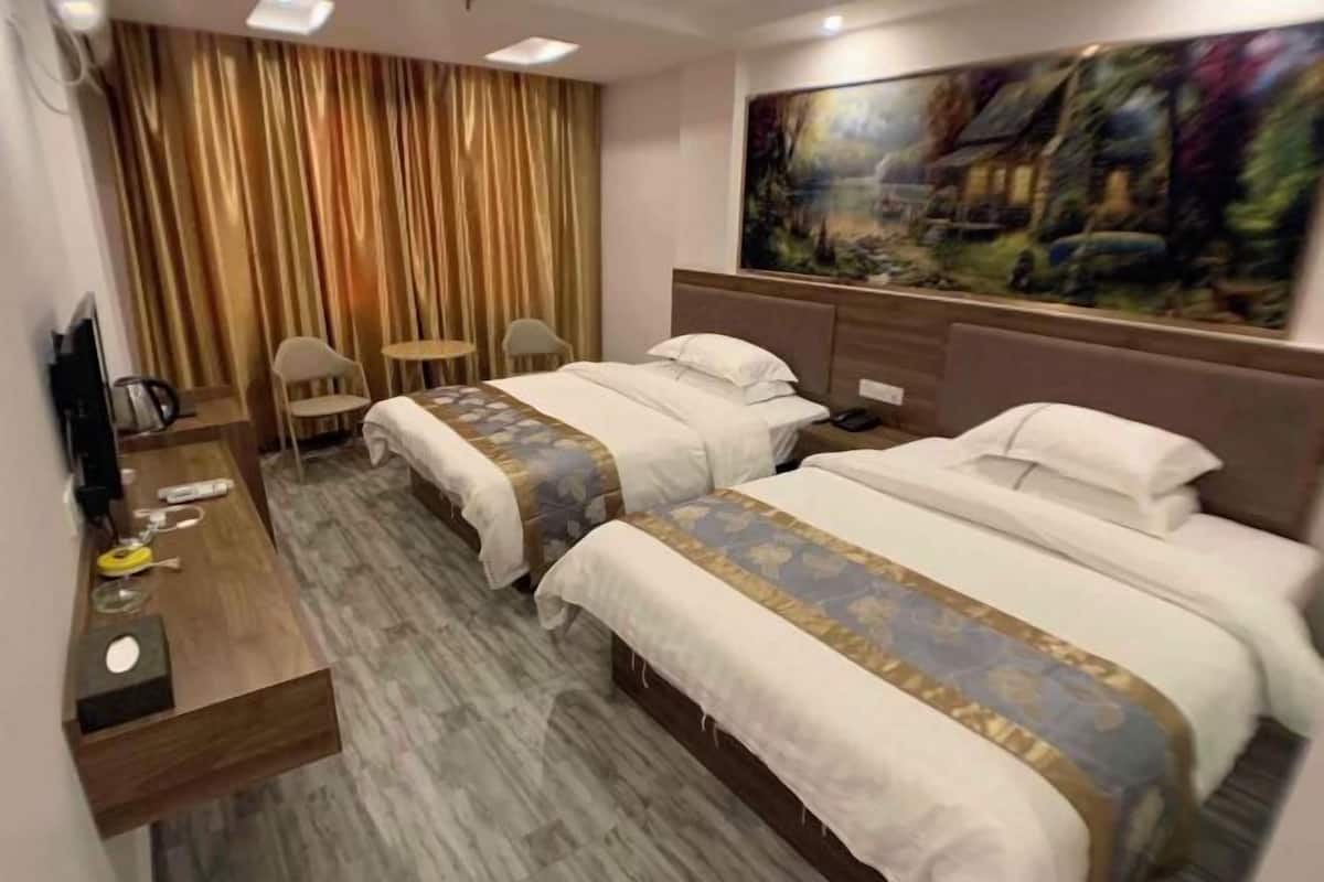 Une chambre d’hôtel avec deux lits, un bureau, une chaise et un tableau au mur.