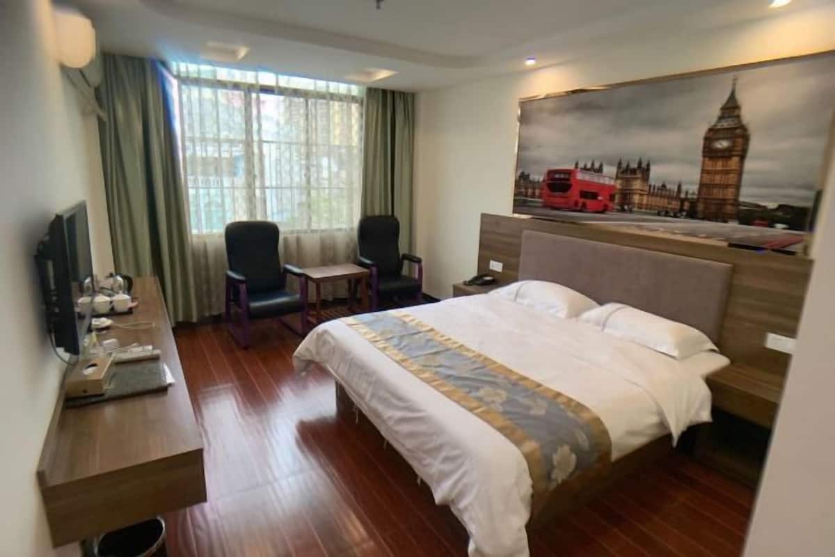 Une chambre d’hôtel comprenant un lit, un bureau avec un ordinateur, une chaise et un tableau représentant des monuments emblématiques de Londres.