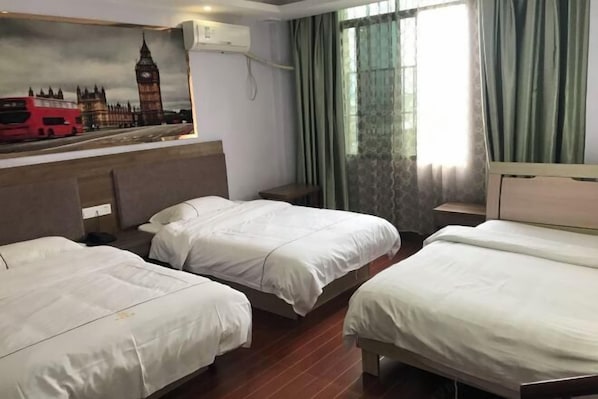 A hotel room with two single beds, a headboard with a painting of London landmarks, a window with curtains, and a bedside table.