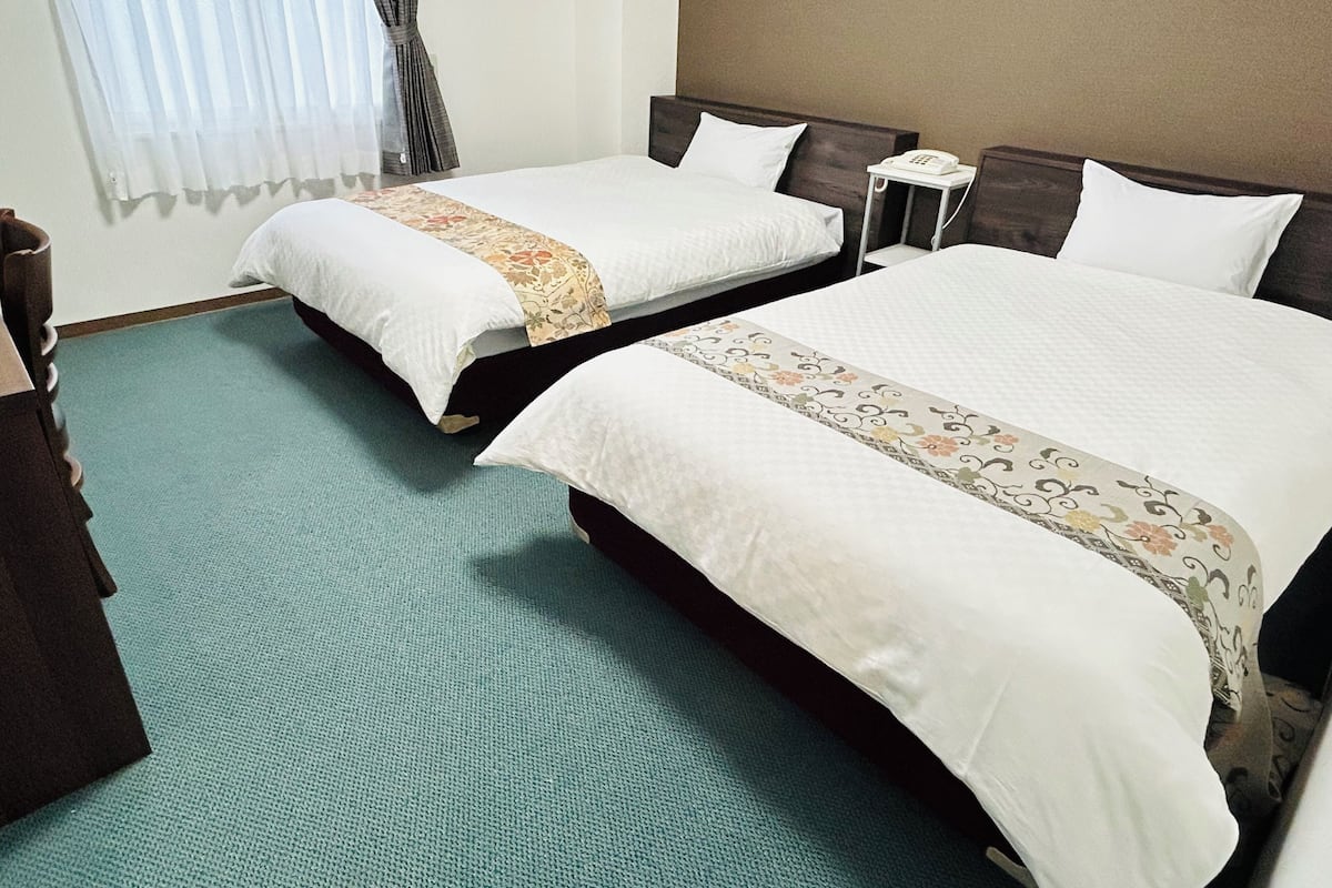 Una habitació d'hotel amb dos llits, una tauleta de nit amb un telèfon i una finestra amb cortines.