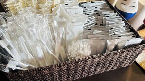 A wicker basket filled with various white plastic items, possibly utensils or tools, and a wooden backdrop with Japanese characters. - GREEN HOTEL AIZU (Aizuwakamatsu)