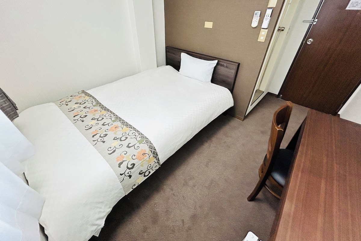 Una habitació d'hotel amb un llit individual, un escriptori de fusta i una porta amb pany.