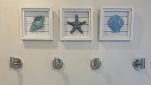 Trois objets décoratifs encadrés sont accrochés au mur : un morceau de corail, une étoile de mer et un coquillage.