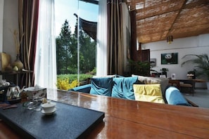 Quarto com sofá, mesa com bandeja e vista para o verde lá fora.