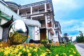 A building with a traditional architectural style, a large reflective sphere, and a well-maintained garden with yellow flowers. - Erhaike Inn (Dali City)