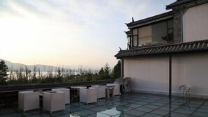 Una terraza en la azotea con un edificio tradicional, mobiliario moderno y vistas a montañas distantes.