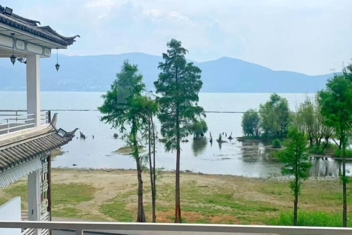 Un bâtiment traditionnel avec un toit en tuiles, offrant une vue sur un lac, des arbres et des montagnes en arrière-plan.