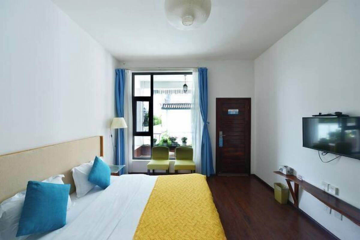 Une chambre d’hôtel avec un lit, une télévision, un balcon avec des chaises et une porte en bois.