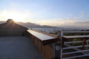 A rooftop terrace with a wooden deck, a white railing, and a view of a body of water and mountains in the distance. - Erhaike Inn (Dali City)