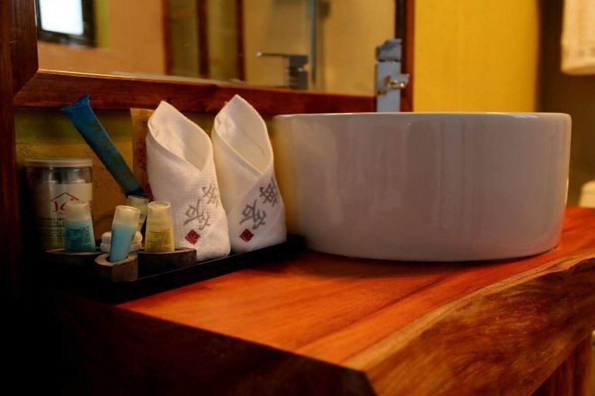 Ein Badezimmer-Waschtisch mit einer weißen Keramikwaschbecken, zwei weißen Handtüchern und Pflegeprodukten.