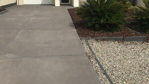 Einbungalow mit Garage, Auffahrt und kleinem Garten mit Pflanzen und Kies.
