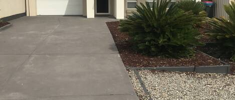 A single-story house with a garage, a driveway, and a small garden area with plants and gravel.