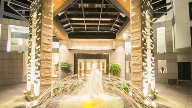 Un hall de hotel con una fuente central, pilares de piedra y un diseño moderno en el techo.