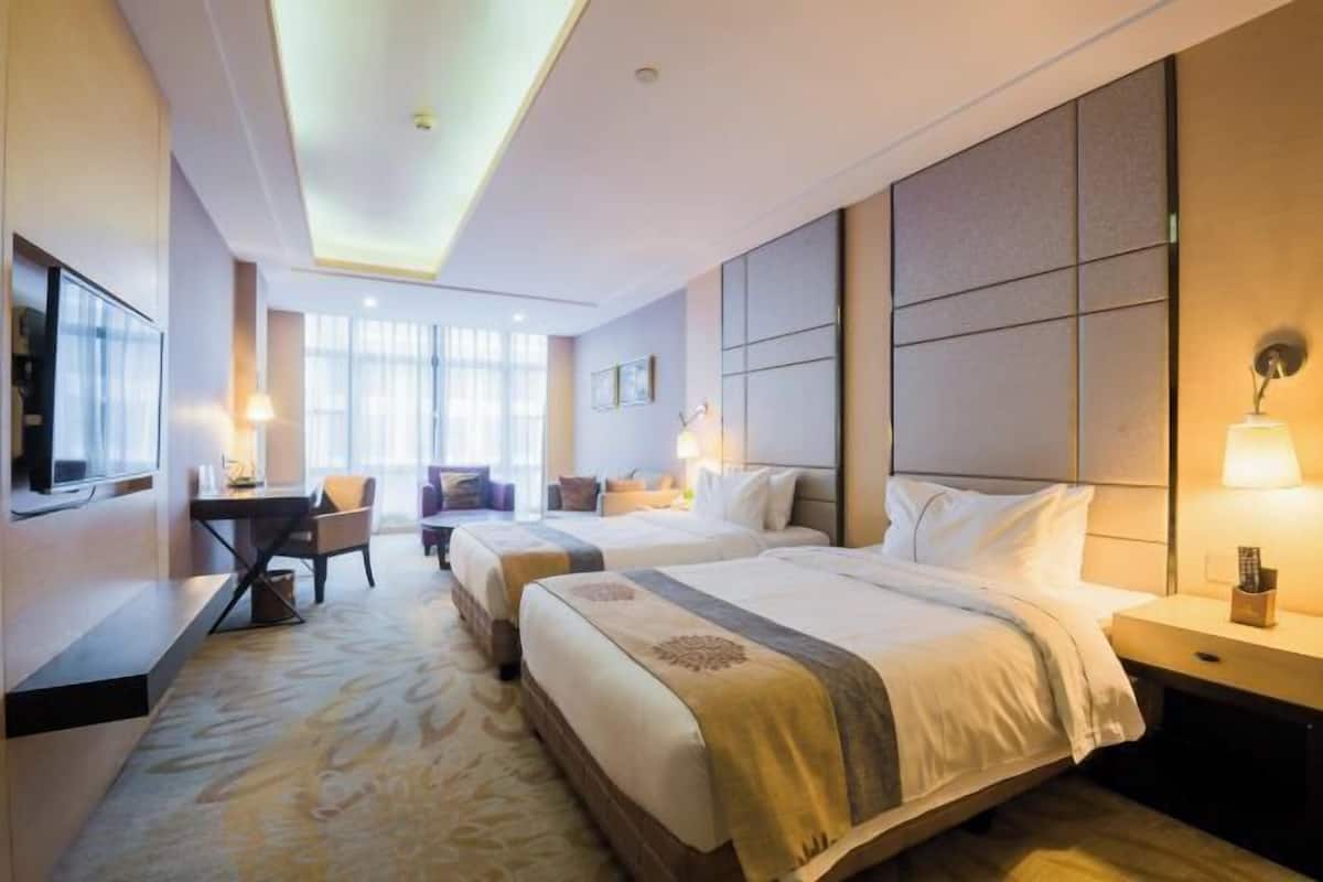 A hotel room with two beds, a desk, and a TV.