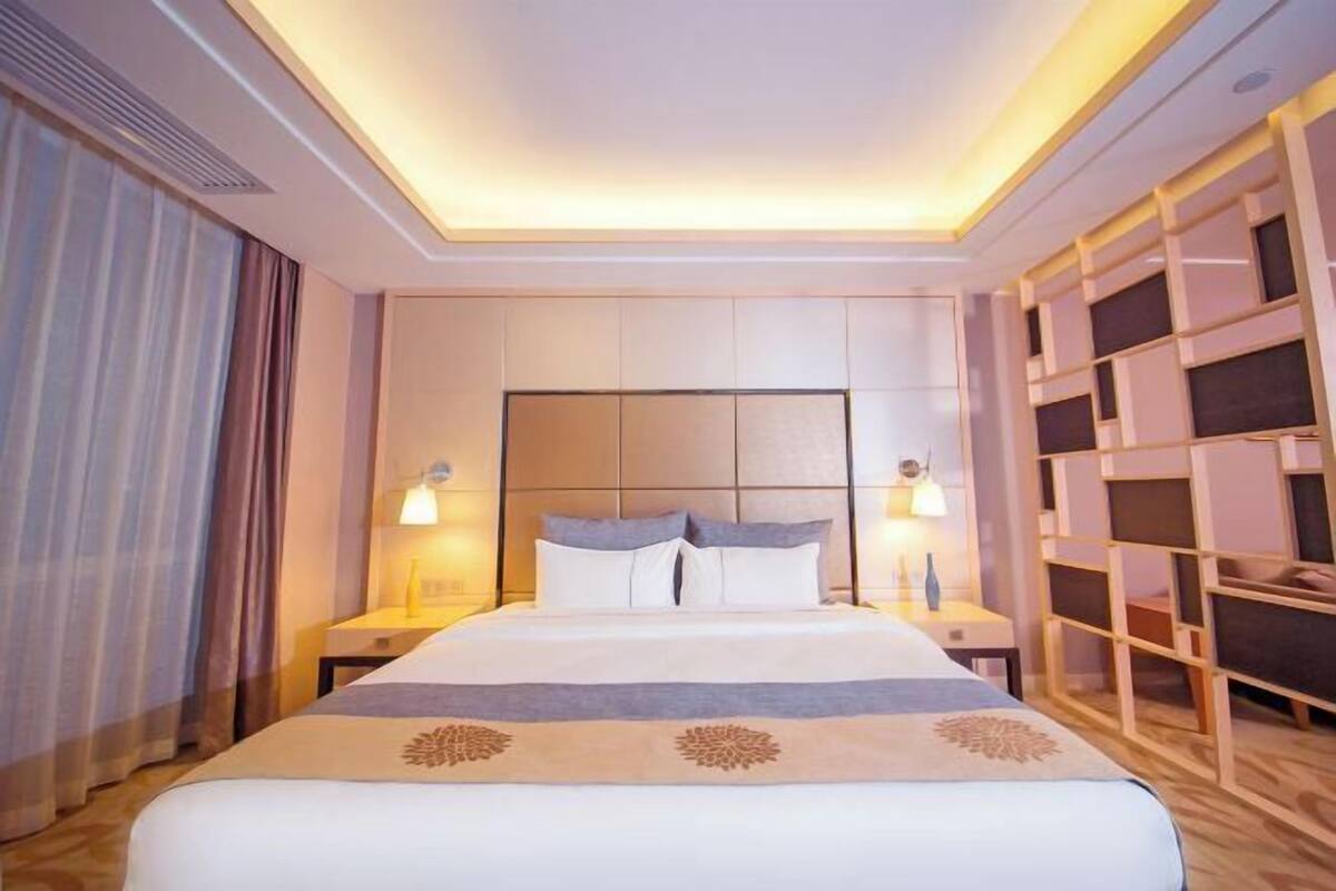 A hotel room with a large bed, bedside lamps, a headboard, and built-in shelving.