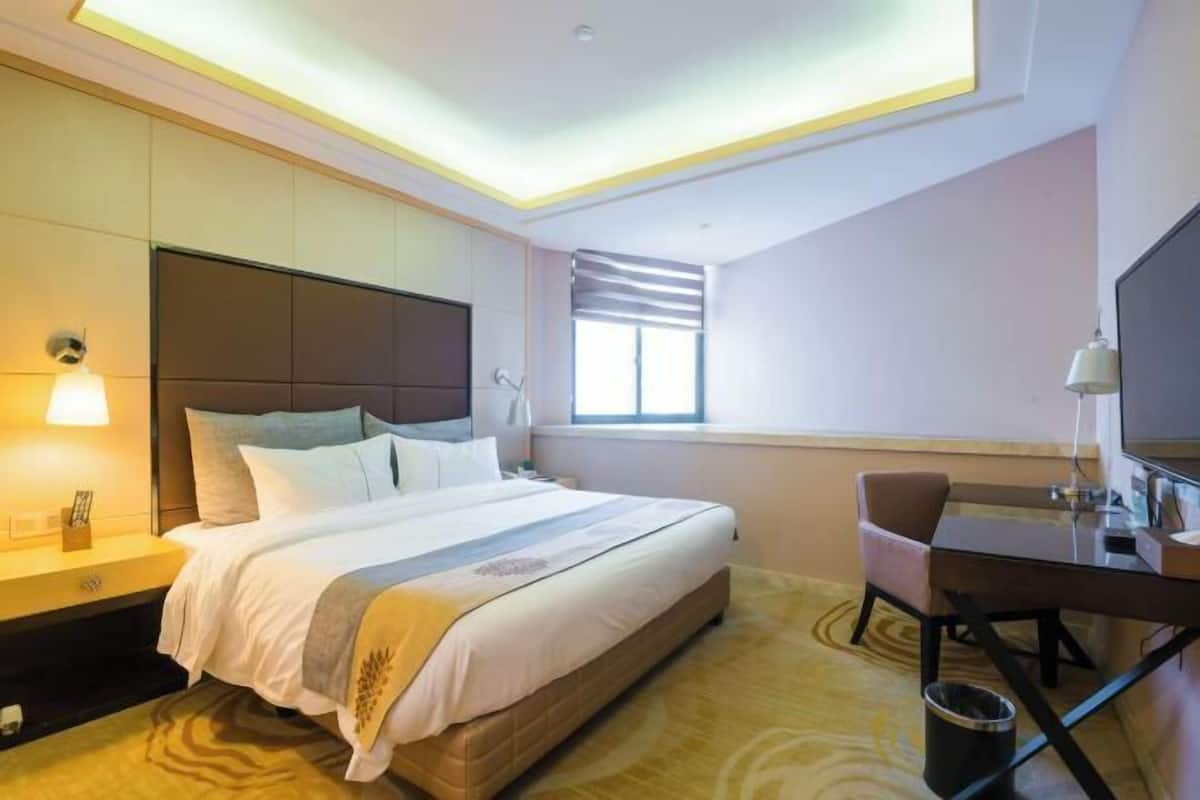 A hotel room with a bed, a desk, a chair, a TV, and a window.