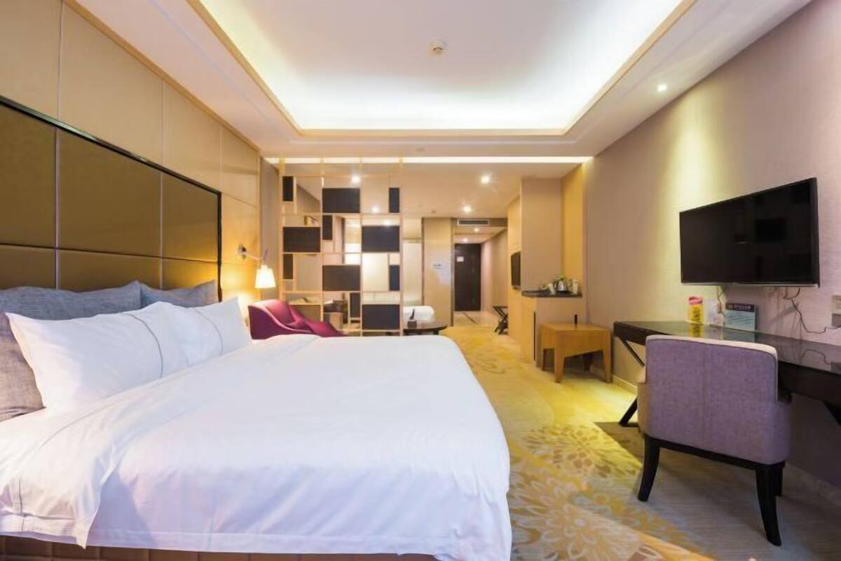 A hotel room with a large bed, a desk, a chair, a TV, and a wall-mounted TV.