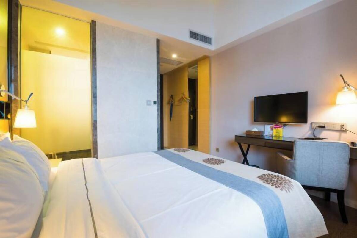 A hotel room with a bed, a desk, a chair, a television, and a mirror.