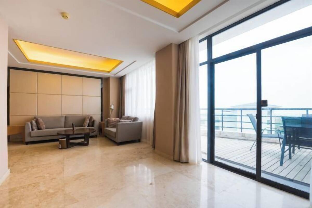 A modern living room with a sofa, a coffee table, and a view of a balcony with outdoor furniture.