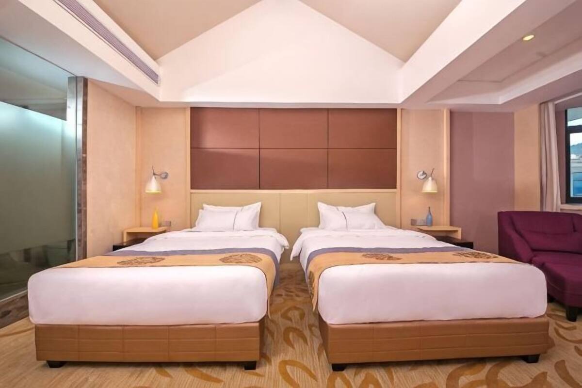A hotel room with two beds, a large padded headboard, bedside lamps, a purple chair, and a view of the city.