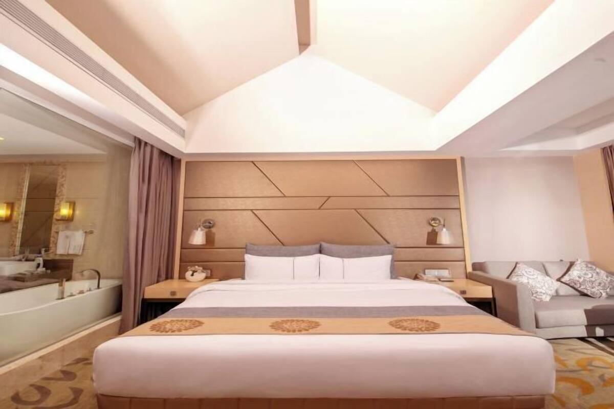 A hotel room with a large bed, a sitting area, a vanity with a mirror, and a bathtub.