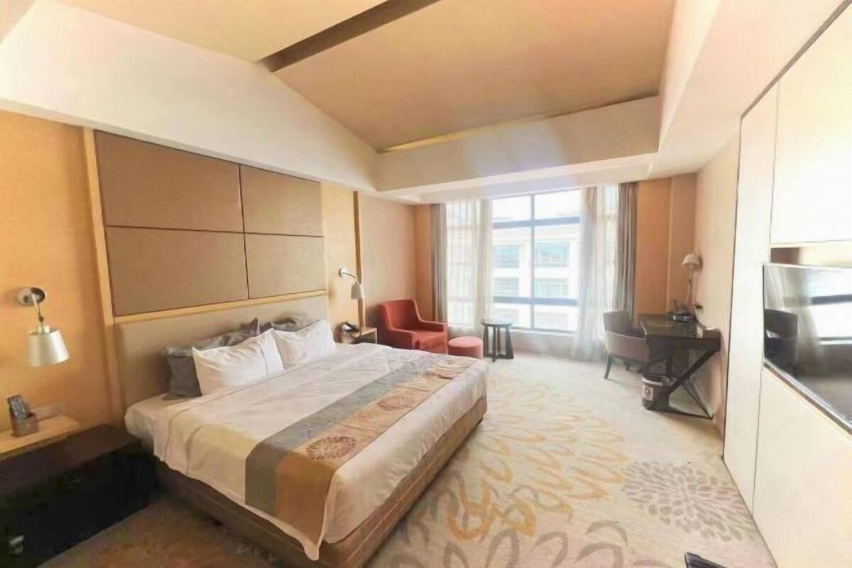 A hotel room with a large bed, a desk, a chair, and a TV.