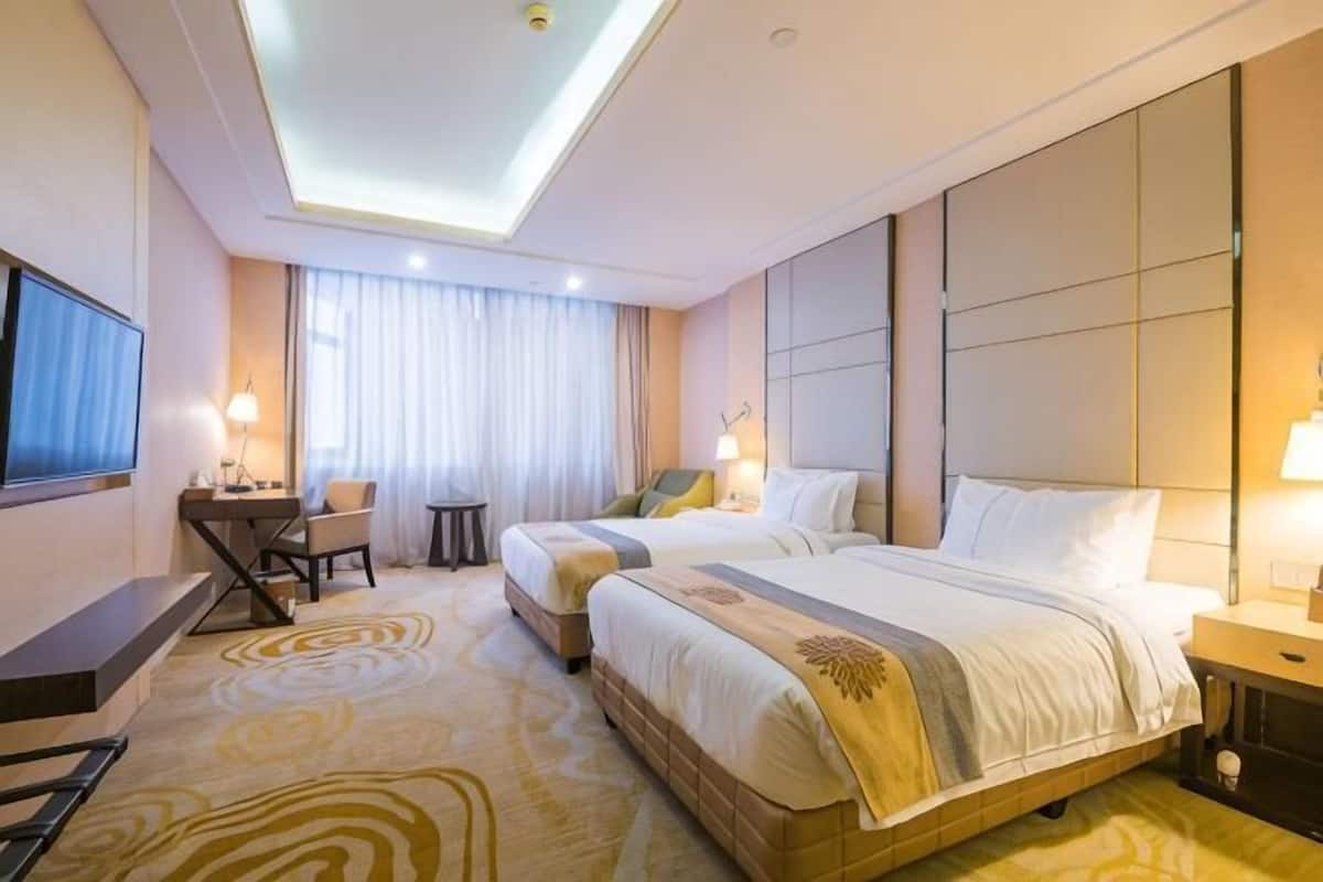 A hotel room with two beds, a desk, a TV, and a large window with curtains.