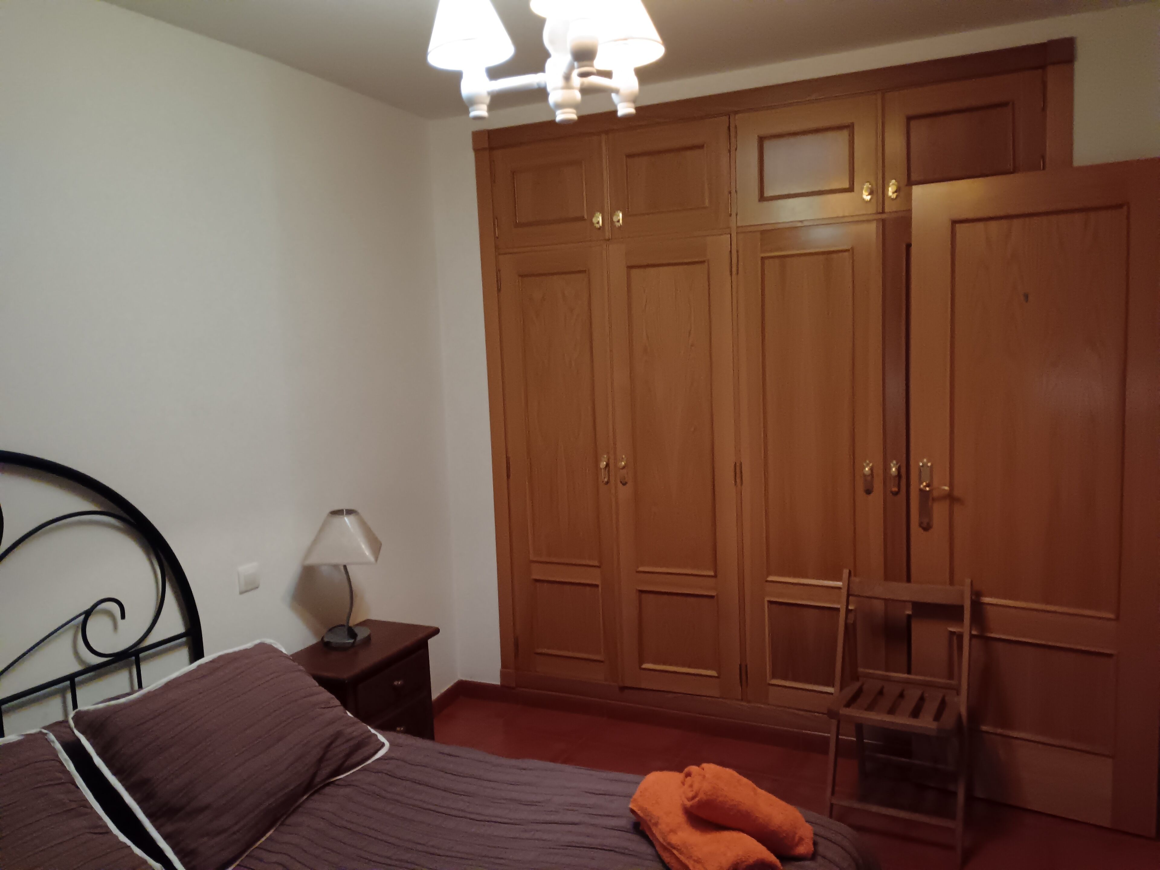 Une chambre à coucher avec un lit, une table de chevet avec une lampe, une armoire en bois et une chaise.