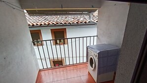 A balcony with a washing machine, tiled floor, and a view of neighboring buildings. - Casa Rural Abuela Maria (Pasarón de la Vera)