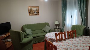 A living room with a green sofa, a TV, a table with a patterned tablecloth, and a lamp. - Casa Rural Abuela Maria (Pasarón de la Vera)