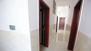 Un pasillo con puertas que dan a habitaciones, suelo de baldosas y una puerta al final.