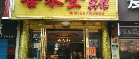 A hotel entrance with a yellow sign, a chandelier, and two potted plants.