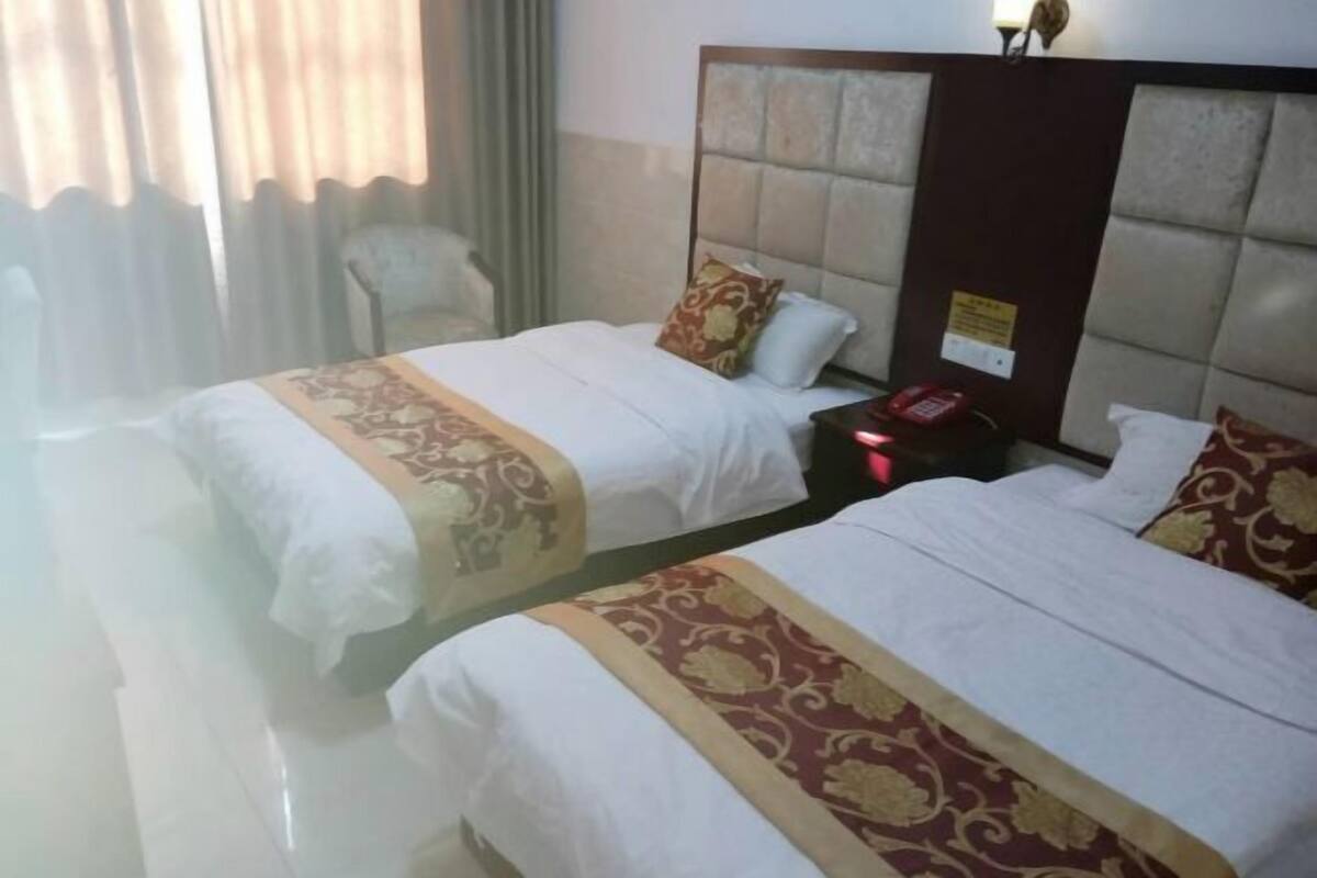 A hotel room with two beds, each with white bedding and decorative headboards. There is a nightstand with a phone and a lamp.
