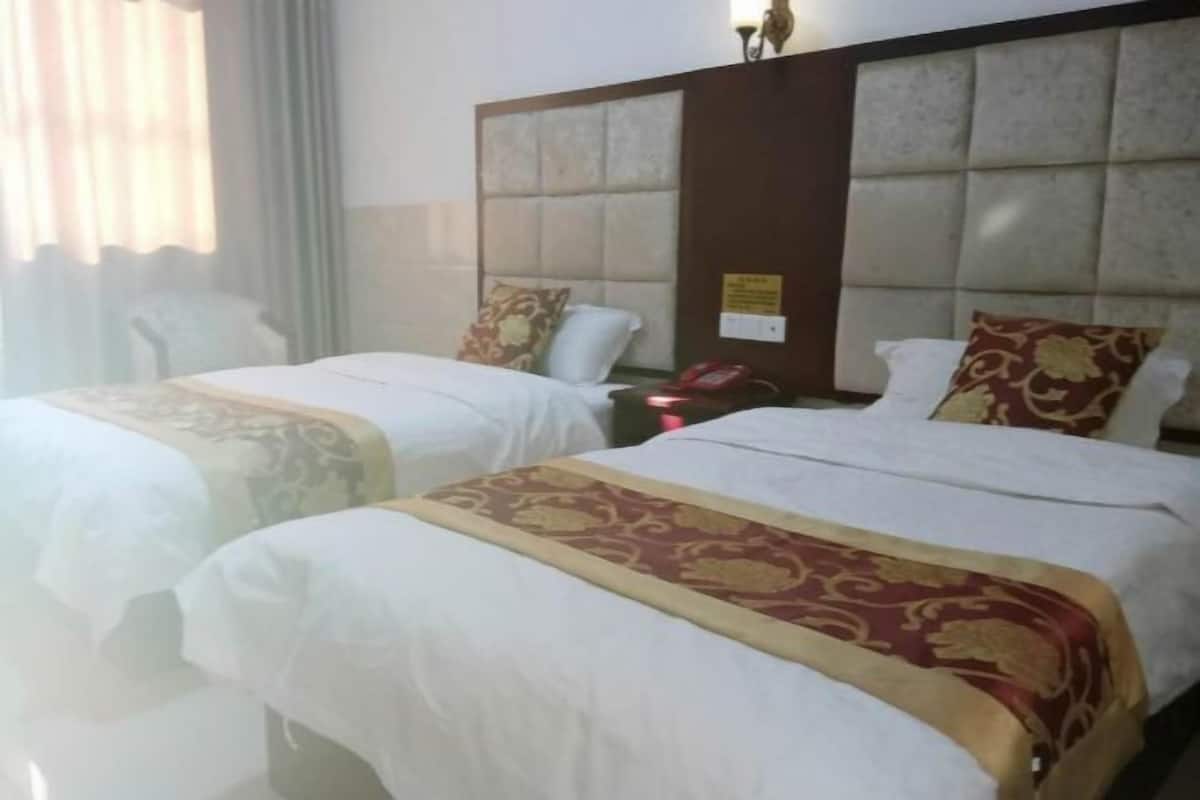 A hotel room with two beds, each with a headboard and a bedside table with a lamp.