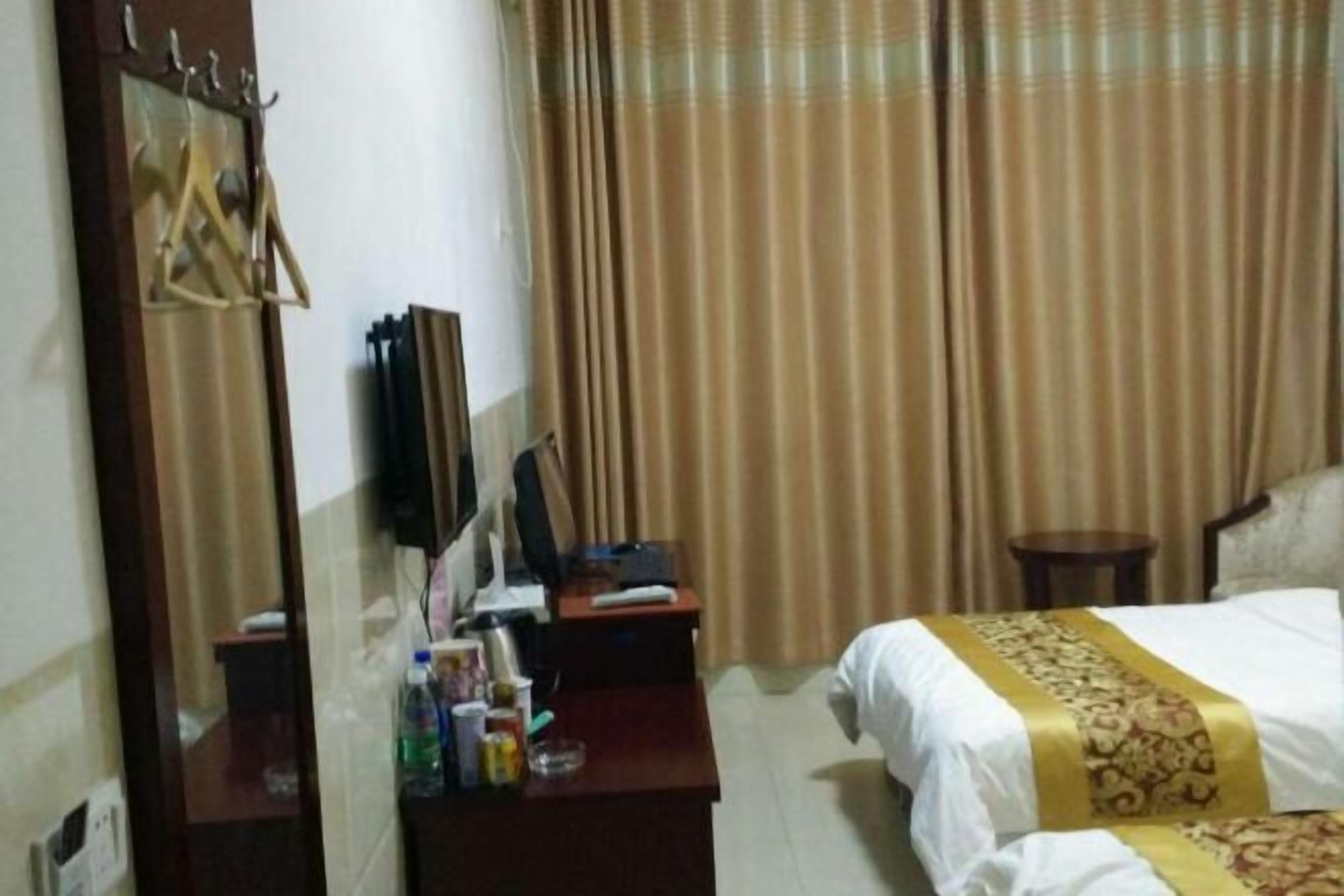 A hotel room with a bed, a desk with a computer, a mirror, and a window with curtains.