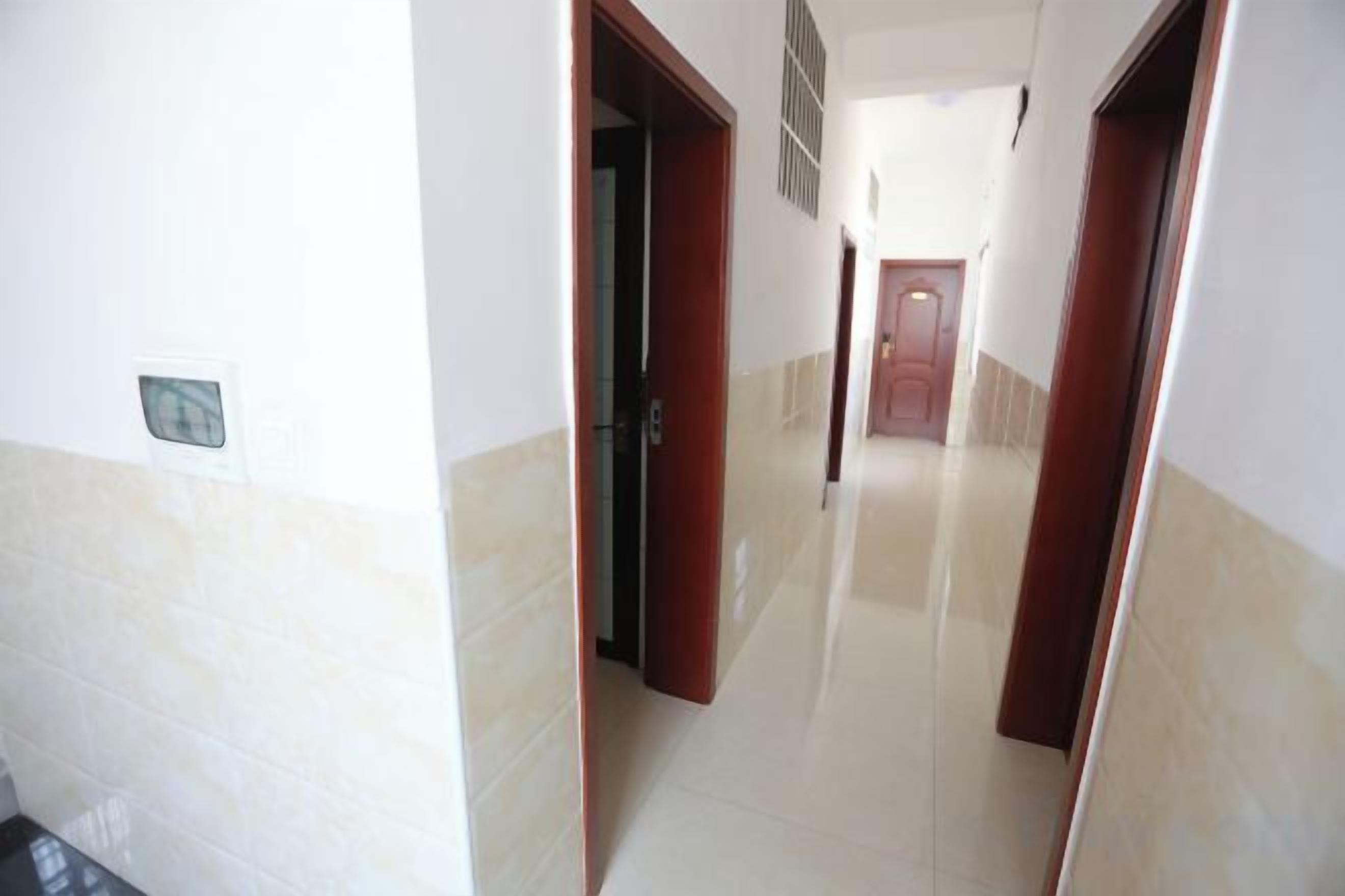 A hallway with a door at the end, a light switch on the wall, and a vent on the ceiling.