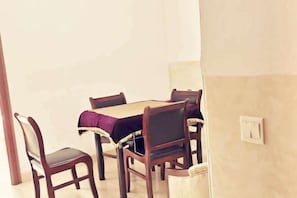 Comedor con mesa de madera y cuatro sillas, mantel morado y un interruptor de luz en la pared.