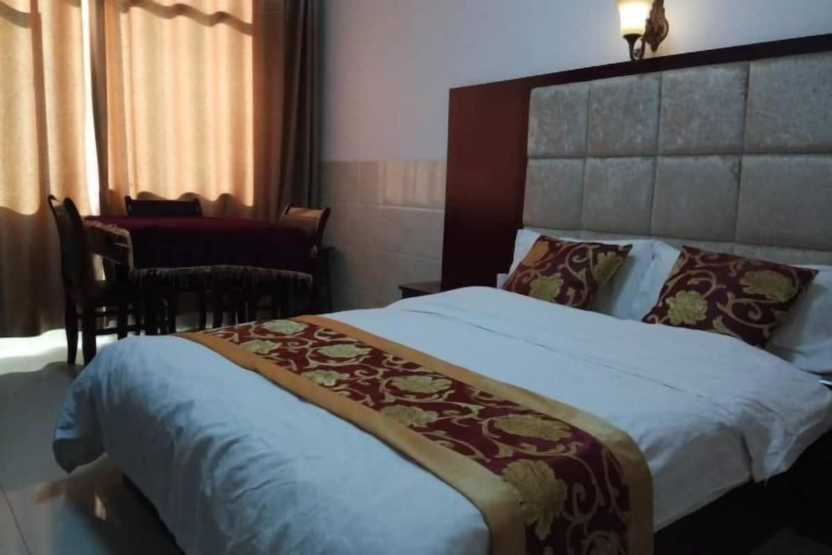 A hotel room with a bed, a table with chairs, and a lamp.