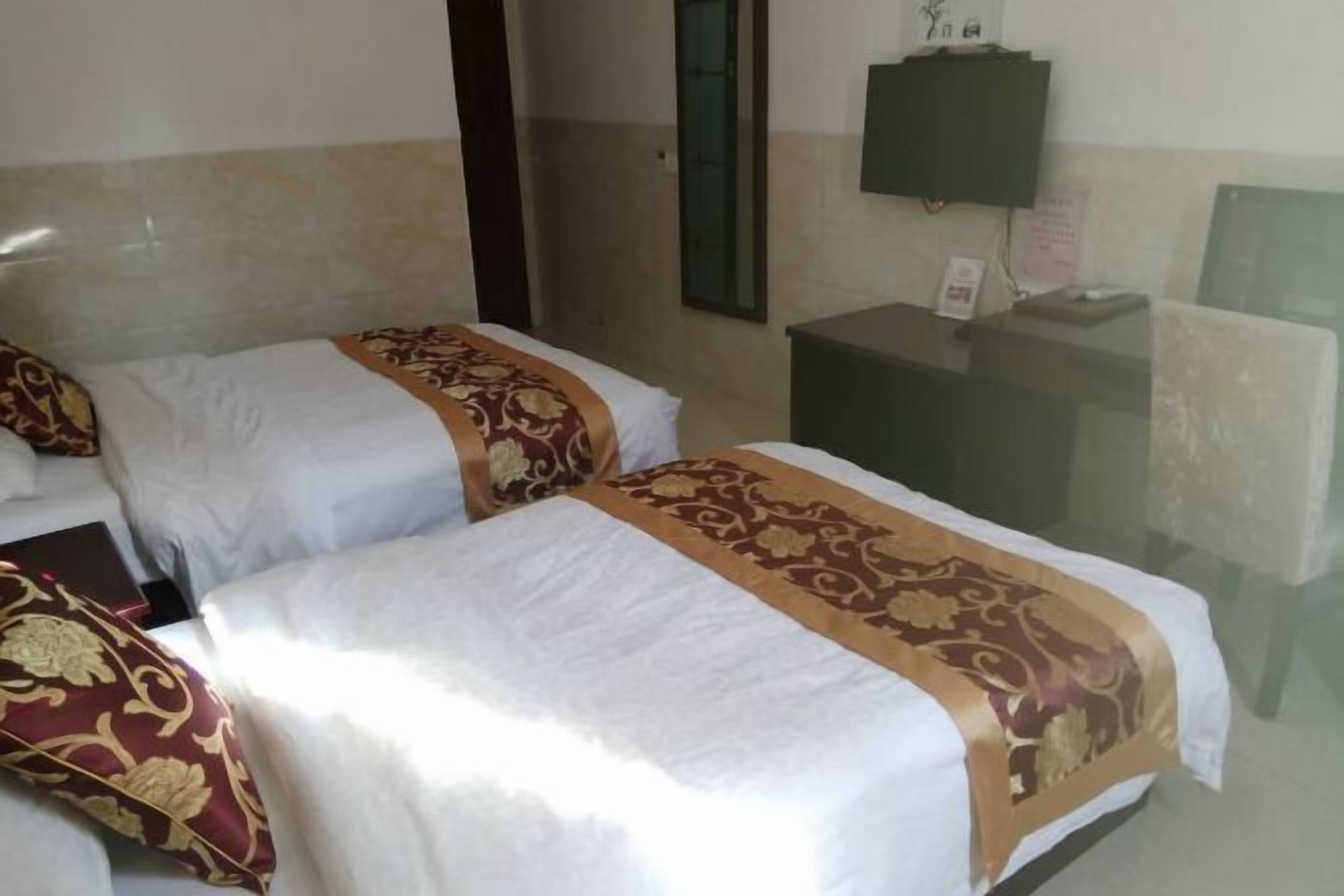 Ein Hotelzimmer mit zwei Betten, jeweils mit weißer und goldener Bettdecke, einem Nachttisch mit Lampe sowie einem kleinen Schreibtisch und Stuhl.