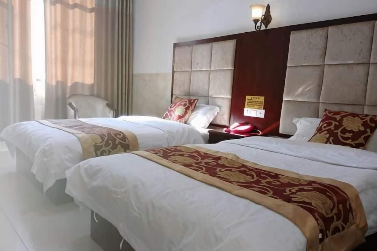 A hotel room with two beds, a nightstand, a chair, and a window with curtains.