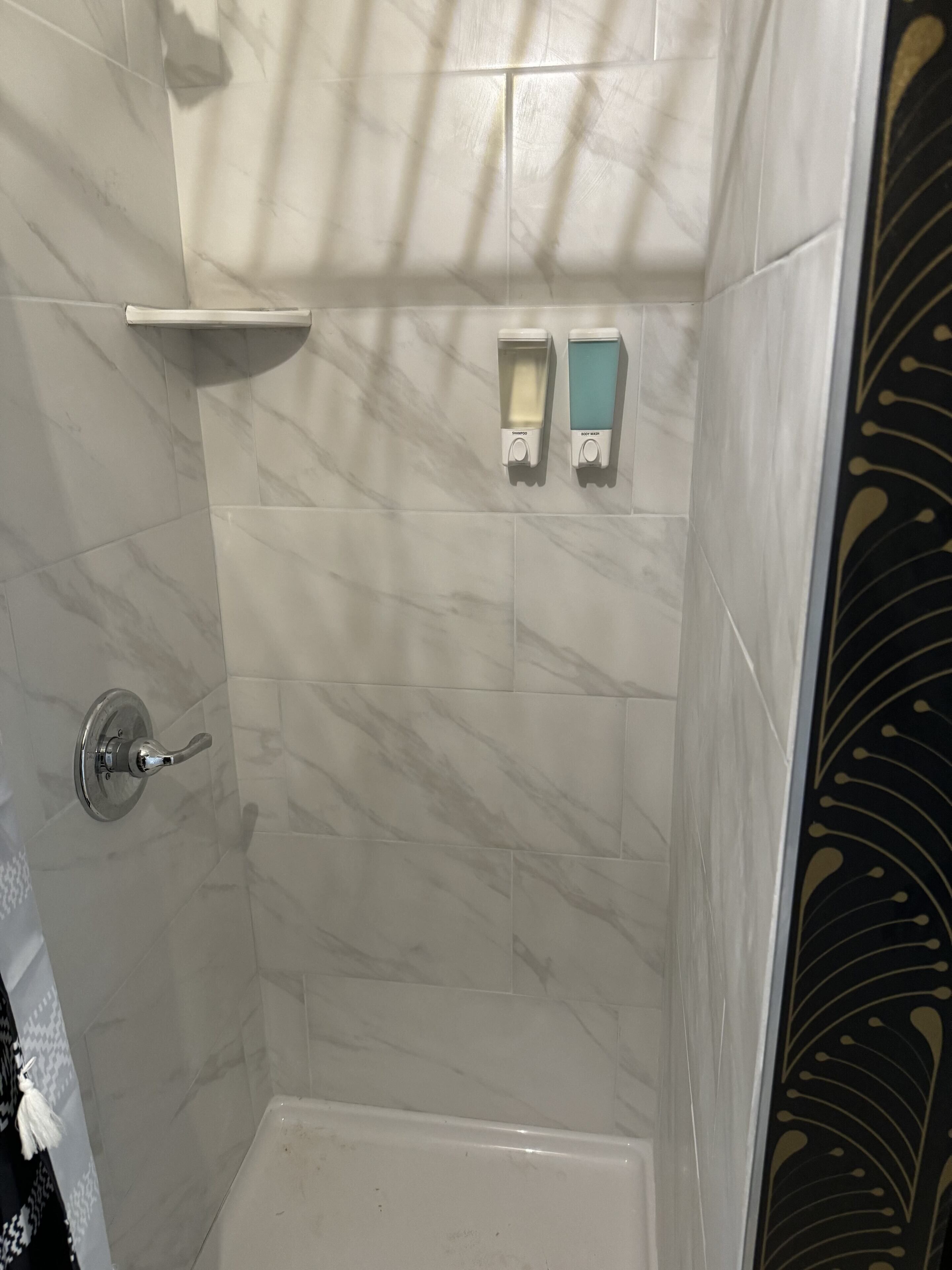 Zona doccia con parete in marmo, soffione e due erogatori di sapone.