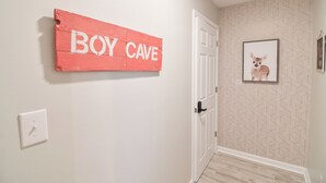 Un couloir avec une porte, une enseigne fixée au mur sur laquelle on peut lire « BOY CAVE », et un tableau représentant un cerf.