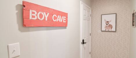 A hallway with a door, a wall-mounted sign reading 'BOY CAVE', and a framed picture on the wall.