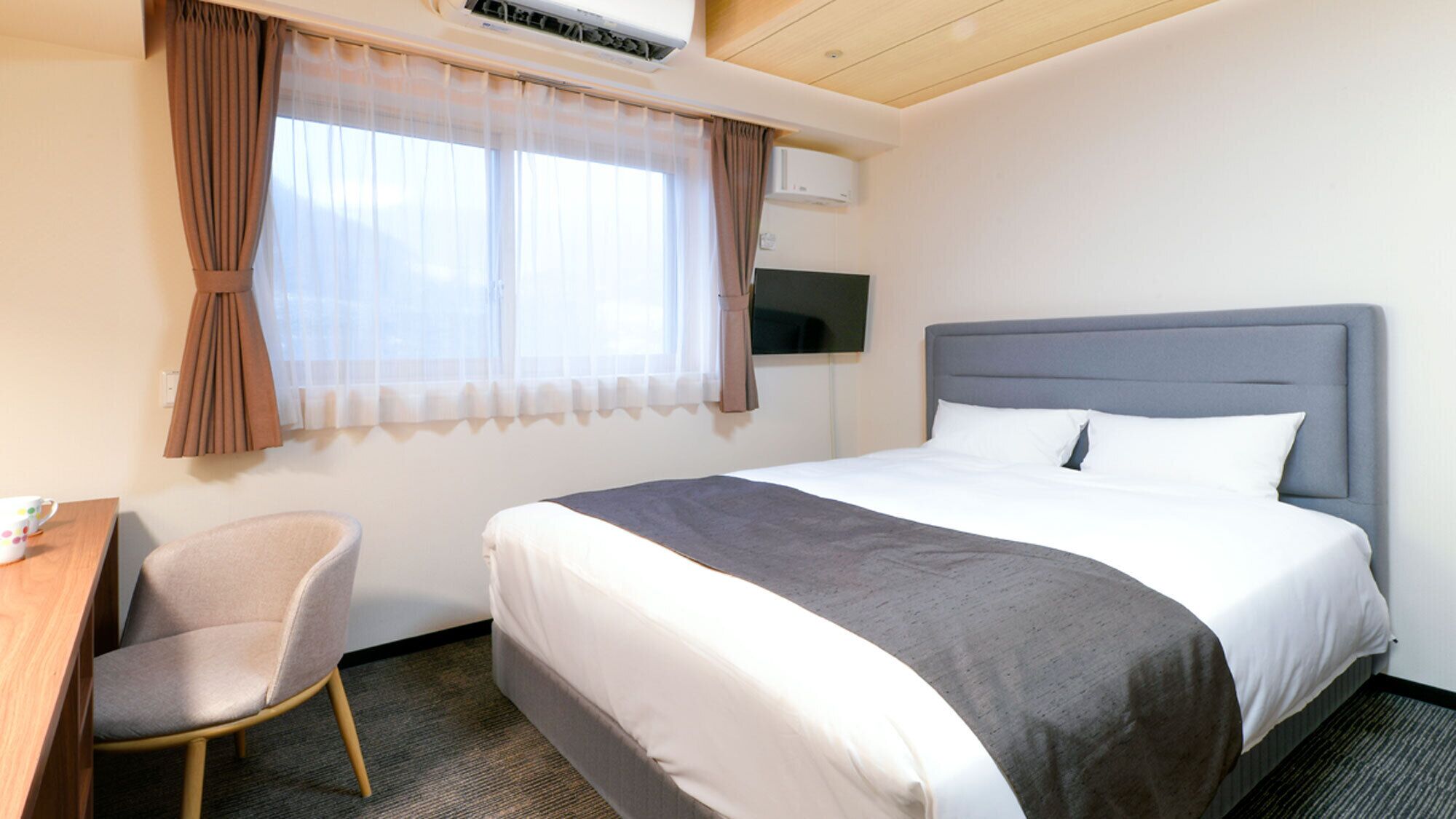 Hotellihuone, jossa on sänky, työpöytä, tuoli ja televisio.