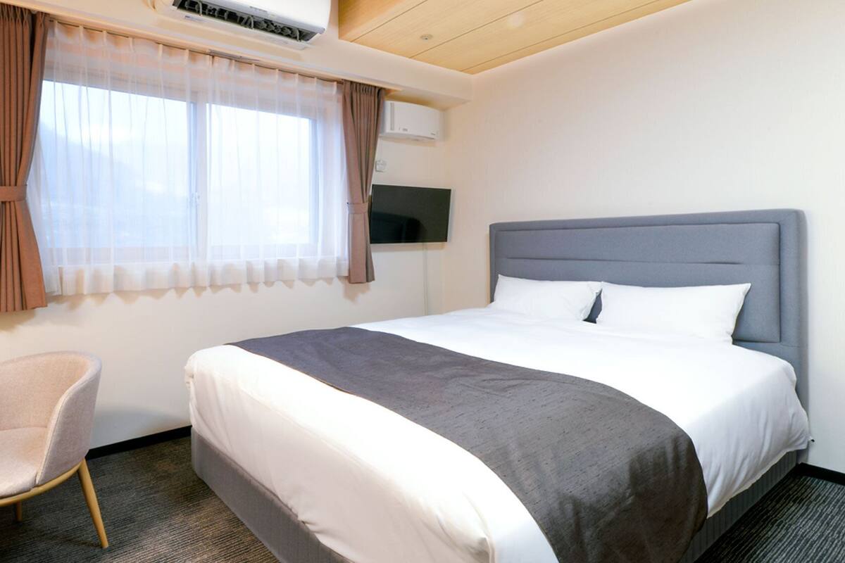 Una habitación de hotel con cama, una silla, un escritorio y un equipo de aire acondicionado.