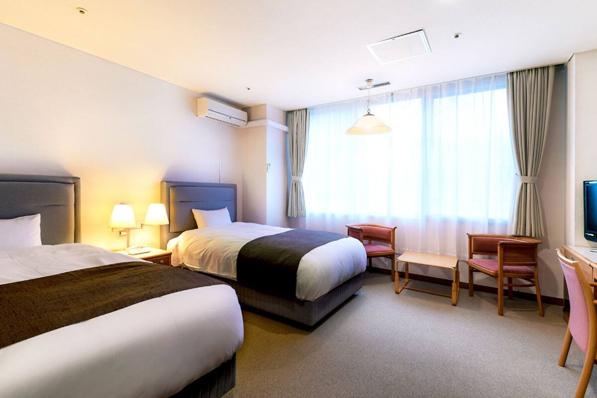 Habitación de hotel con dos camas, un escritorio, una silla y un televisor.