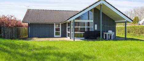 A modern house with a large glass door, a covered patio, and a fenced yard.