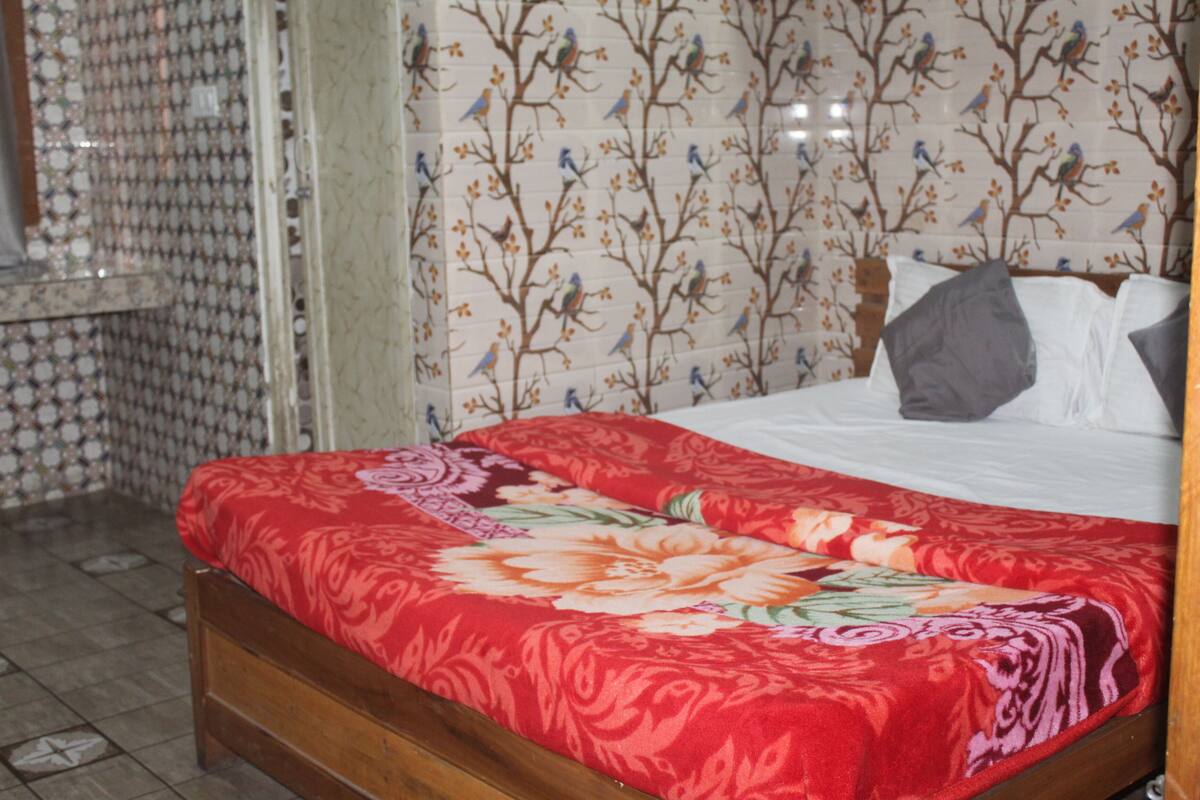 A bedroom with a wooden bed, floral bedspread, and patterned wallpaper.